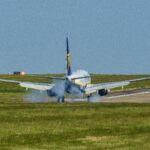 A commercial aircraft touches down on a runway at Leeds airport, UK, amidst clear skies.