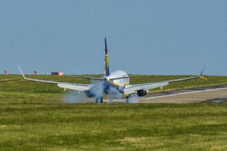 A commercial aircraft touches down on a runway at Leeds airport, UK, amidst clear skies.
