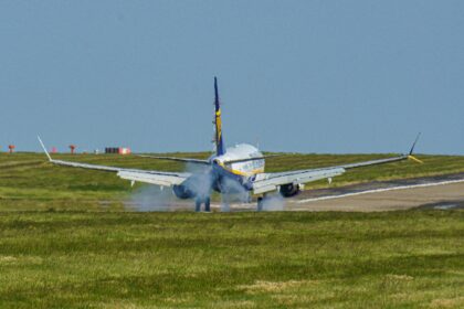 A commercial aircraft touches down on a runway at Leeds airport, UK, amidst clear skies.