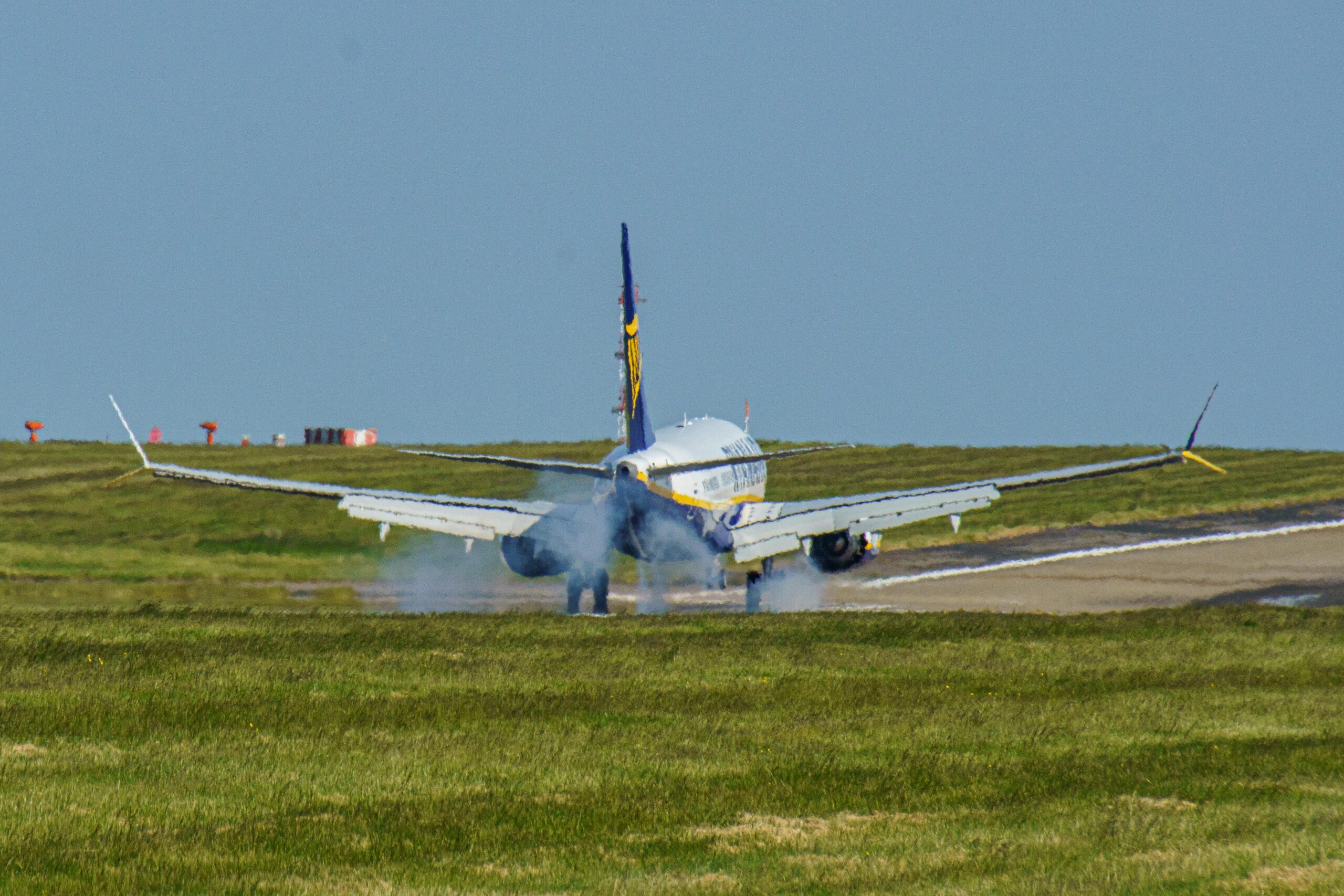 A commercial aircraft touches down on a runway at Leeds airport, UK, amidst clear skies.