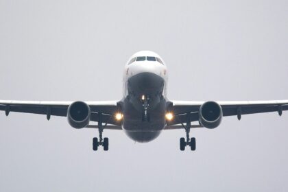 A commercial airliner captured head-on, preparing to land against a cloudy sky.